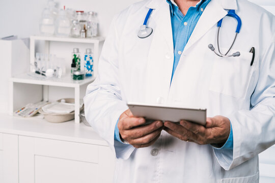 Unrecognizable cropped medic in robe using tablet in clinic