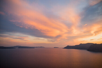 Majestic scenery of calm rippling sea near rough hills beneath cloudy pink sunset sky in Santorini Greece