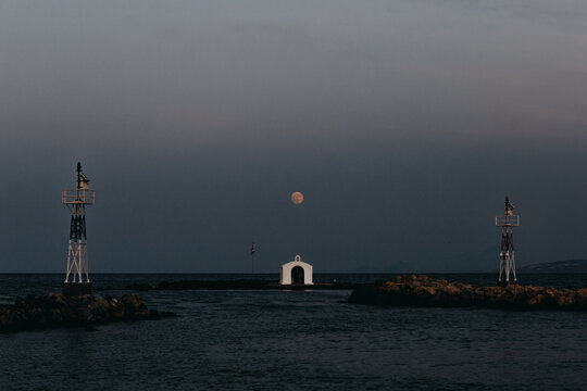 Scenic view of small white St Nickolas Church located on islet under dark sky with luminous moon at dusk