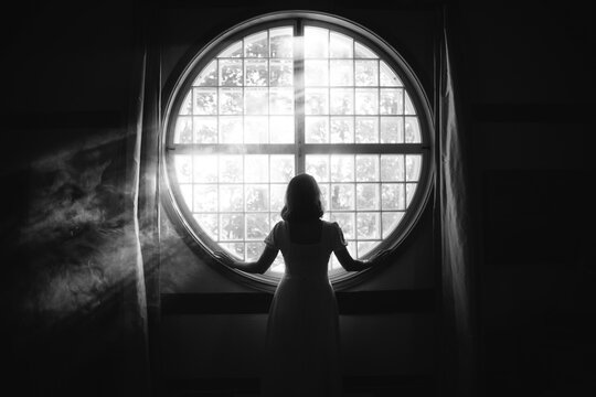 Back view of unrecognizable gentle female touching fence on round shaped window in house in sunlight