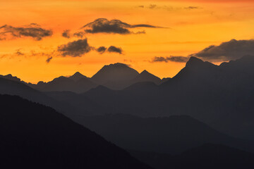 Breathtaking view of silhouettes of mountain peaks on background of bright orange sundown sky
