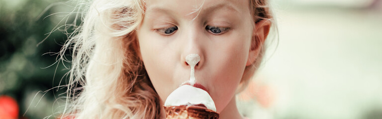 Cute funny adorable girl with dirty nose eating licking ice cream. Kid looking at food with crossed...