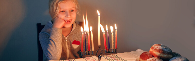 Girl lighting candles on menorah for traditional winter Jewish Hanukkah holiday. Child celebrating...