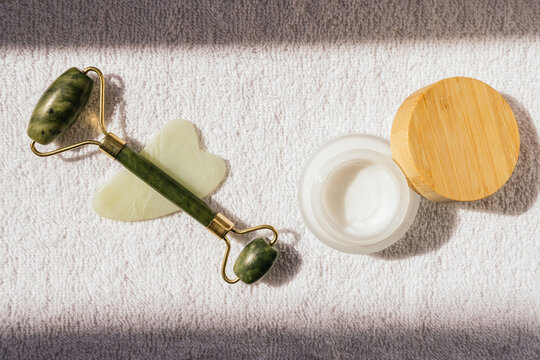 High angle of jade roller and guasha scraper placed on towel and natural facial cream in spa salon