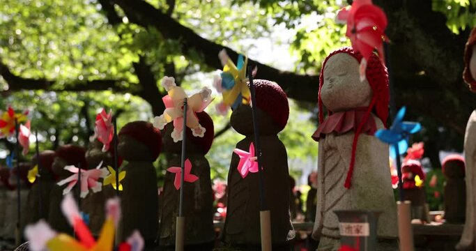 A slow motion of moving colorful windmills with Jizo statue daytime