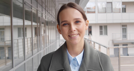 Happy positive young businesswoman in formal wear standing outdoors business center