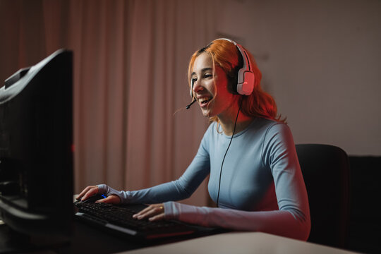 Side view of delighted female gamer in headphones playing videogame while sitting at table at home