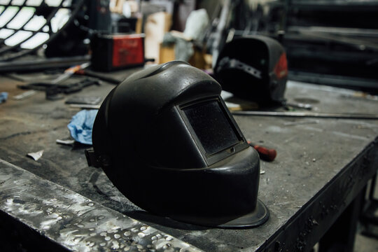 Metal table with welding mask near stationery coil with electric wire in professional garage