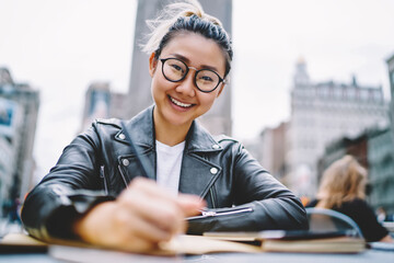 Portrait of happy Chinese tourist sitting in street cafe and smiling at camera enjoying leisure...