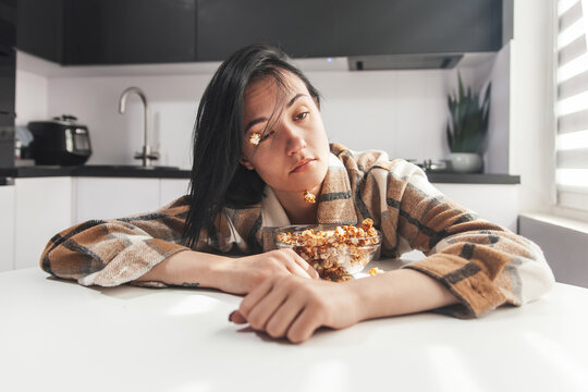 Young sleepy woman waking up in the kitchen with popcorn stuck on her face