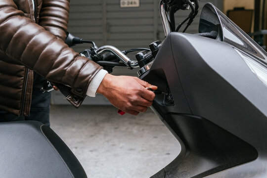 Crop unrecognizable male motorcyclist in leather jacket inserting ignition key into modern bike in city