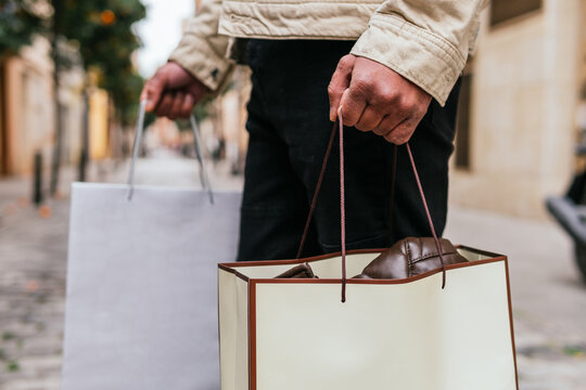 Cropped unrecognizable man with shopping bags strolling on urban walkway