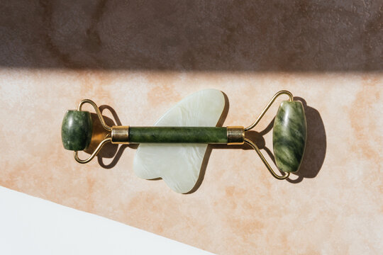 Top view of jade roller and guasha scraper arranged on marble table for concept of face massage