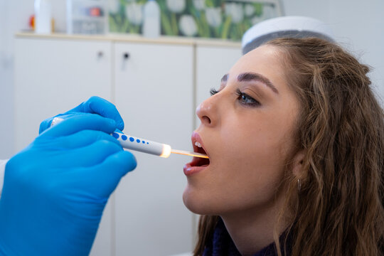 Side view of cropped unrecognizable otolaryngologist in latex gloves checking throat of patient with sterile spatula and flashlight in hospital
