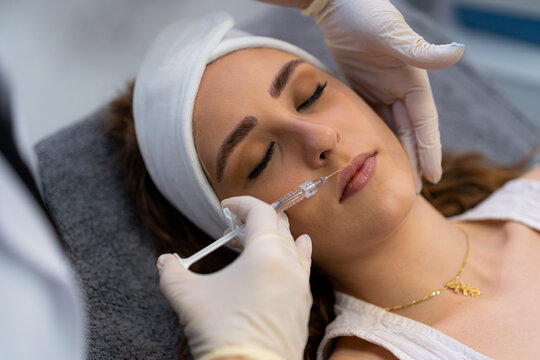 From above of crop unrecognizable professional beautician with syringe injecting filler with hyaluronic acid in lips of female client during procedure in beauty clinic