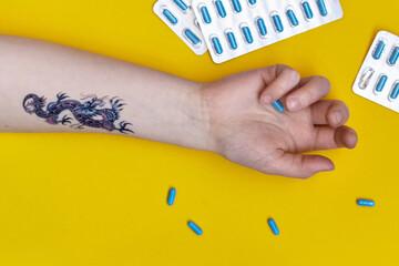 Female hand with a tattoo on a yellow background with scattered sleeping pills. Insomnia,...