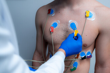 Crop anonymous medic connecting electrodes to chest of male patient for conducting ECG diagnostic of heart