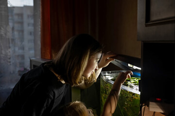 A young woman and a little girl feed fish in a home aquarium