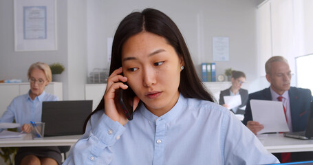 Asian young woman sitting at desk working and answering phone call