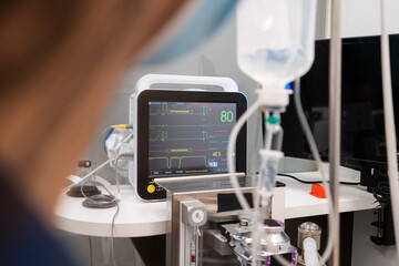 Side view of crop anonymous female veterinarian in mask against professional medical device with graphics and numbers on screen