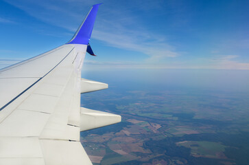 Fototapeta premium White airplane wing on the background of agricultural fields and forests