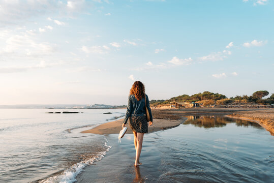 Back view of female walking in water of sea and admiring spectacular view of colorful sundown sky in summer
