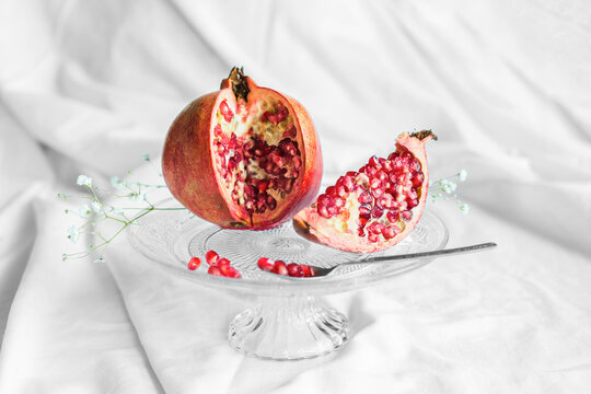 Bright tasty fresh pomegranate with ripe seeds and blooming flower sprig on transparent stand on crumpled fabric