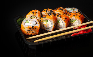 Traditional sushi and chopsticks. Philadelphia with salmon, avocado and cheese. Japanese cuisine on black background