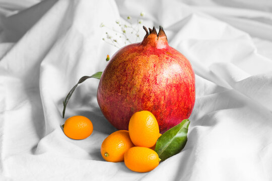 Bright whole fresh pomegranate with cumquats and leaves with sprigs on creased fabric on white background