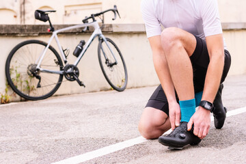 Crop unrecognizable male bicyclist in sports clothes and modern cycling shoes squatting on roadway against bike