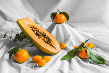 Half of pawpaw with seeds between tangerines and cumquats with leaves on white crumpled cloth