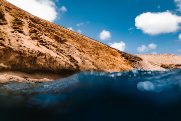 Low angle of clear seawater washing rocky cliff on coast under blue sky with clouds