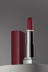 Open dark red lipstic on gray background and concrete podium