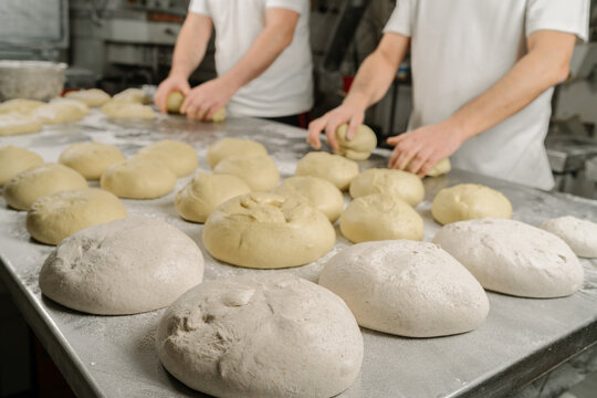 Cropped unrecognizable bakers forming bread from dough at table with flour and bowl in bakery