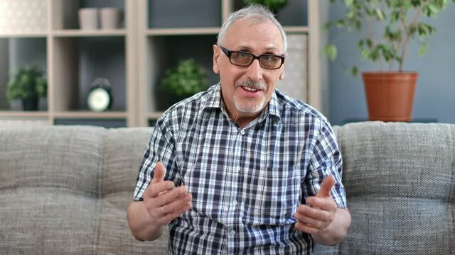 Portrait of smiling grandfather 80s blogger talking gesticulating online broadcasting on couch