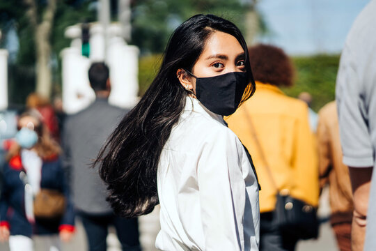 Back view of Asian female with flying hair wearing protective mask walking in crowd and looking at camera