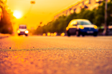 Fototapeta premium Sunset in the city, the cars driving on the road. Close up view from the asphalt level