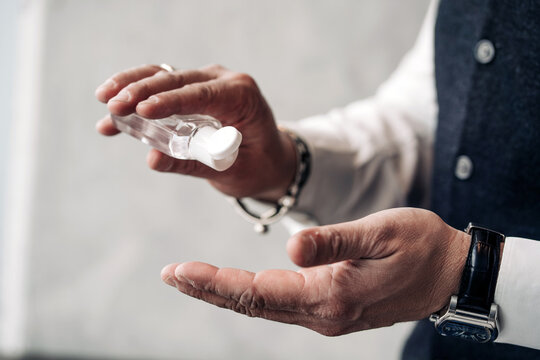 Crop anonymous male entrepreneur in formal wear and wristwatch using disinfectant gel from bottle during coronavirus period