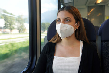 Travel safely on public transport. Young woman with KN95 FFP2 face mask looking through train...