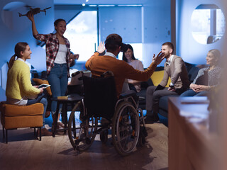 Disabled businessman in a wheelchair at work in modern open space coworking office with team using...