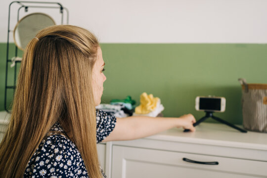 Side view of young female blogger with brown hair and cellphone on commode in light house room