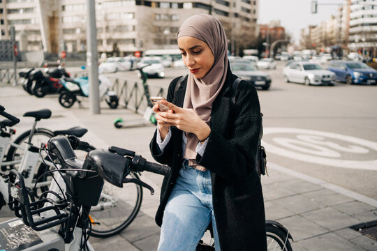 Side view of Muslim female in headscarf using bicycle sharing system in city
