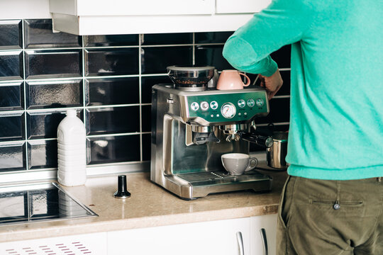Back view of crop unrecognizable male preparing coffee with modern espresso machine at table in house kitchen