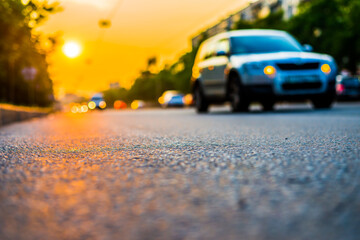 Fototapeta na wymiar Sunset in the city, the car rides near. Close up view from the asphalt level