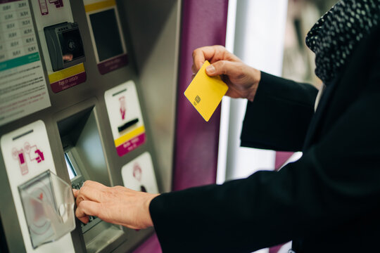 Side view of cropped unrecognizable female standing near ATM machine with card while buying train ticket while standing in modern terminal