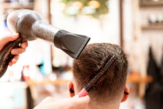 Anonymous stylist with hair dryer against man in cape in armchair in barbershop