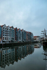A panoramic view on the shores of Martwa Wisla flowing through Gdansk in Poland. The buildings reflect in the calm surface of the river. New architecture meeting with medieval constructions. Overcast