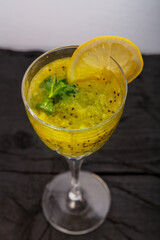 Kiwi smoothie garnished with mint and lemon in a glass on a black background.