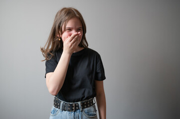 Portrait of teenage girl covering her face with hands on gray background