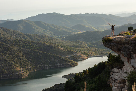 Remote view of female hiker standing with outstretched arms on edge of hill and enjoying freedom during trekking in mountains in summer